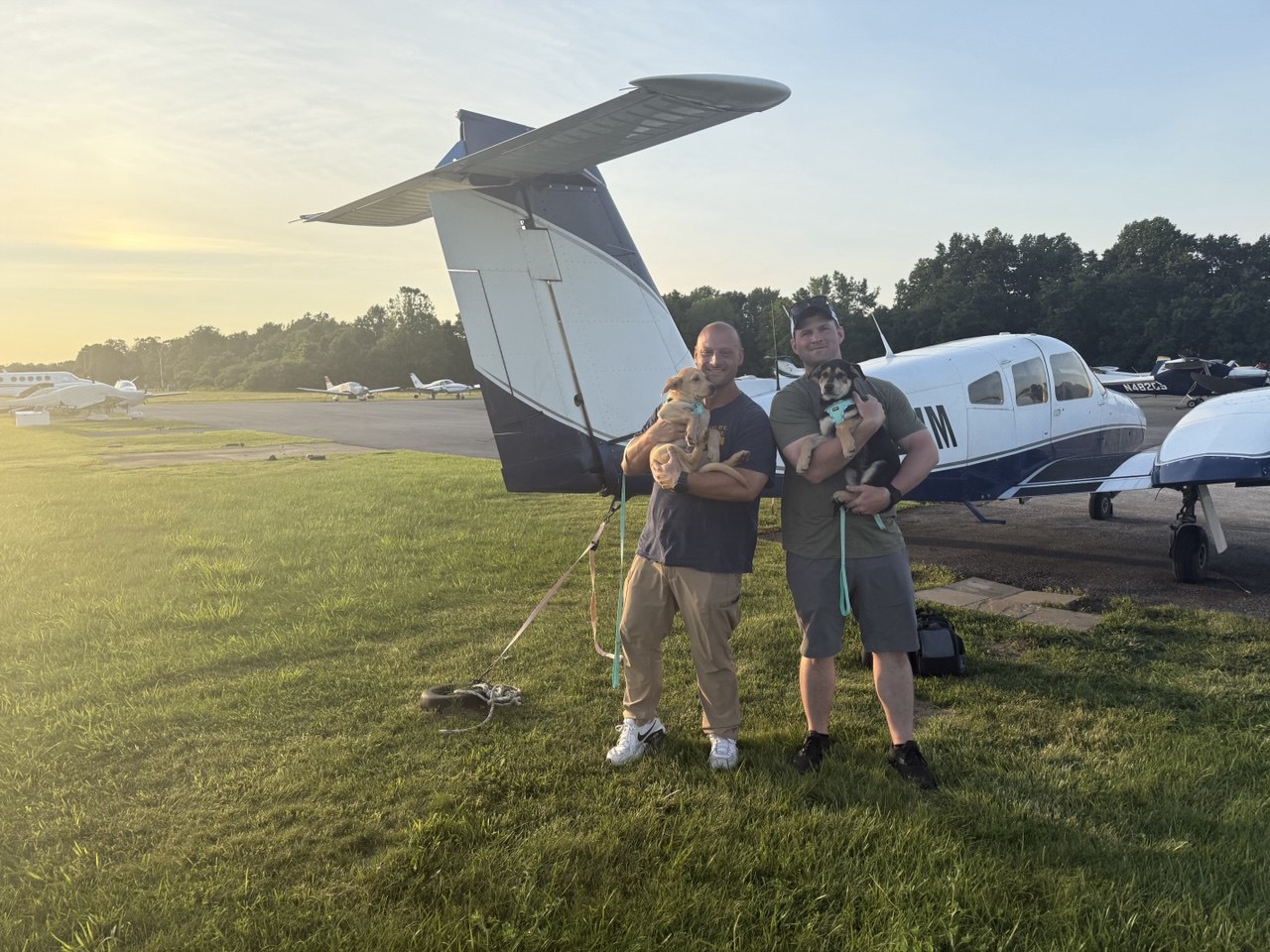 Two pilots holding puppies at golden hour sunset