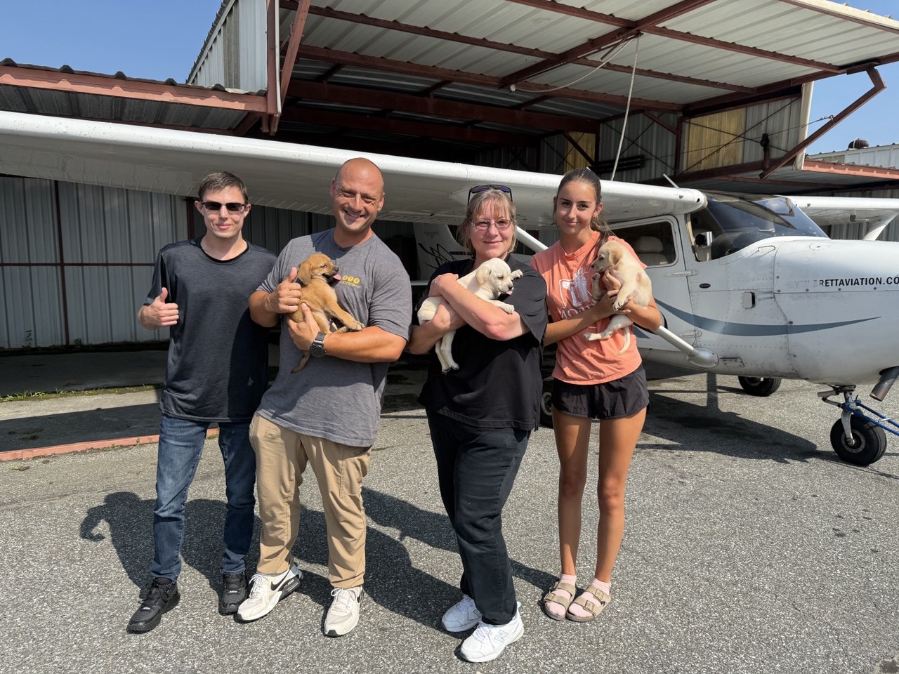 Volunteer team holding puppies in front of a plane at Barrett Aviation hangar