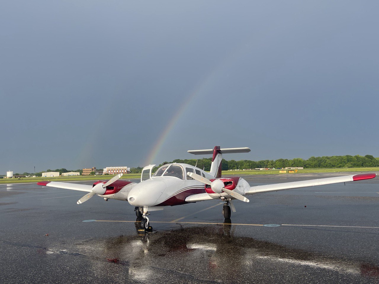 Red and white twin-engine plane on a rain-soaked ramp with a rainbow behind it