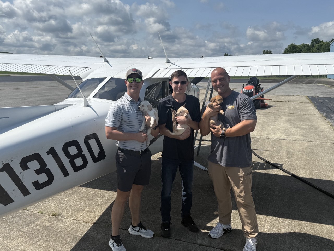 Three volunteer pilots each holding a puppy in front of a Cessna
